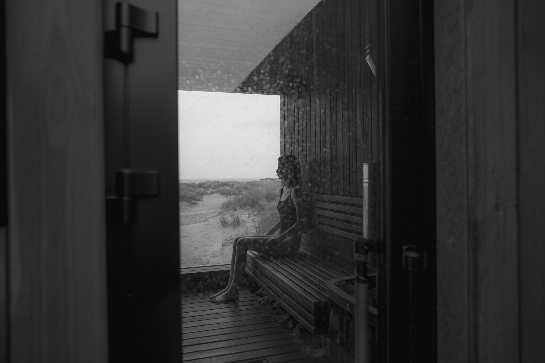Person sitting on wooden bench inside a small indoor cedar sauna